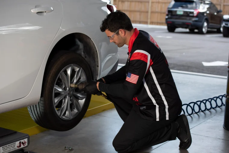 Technician tightening a car wheel with an impact wrench in a service bay.